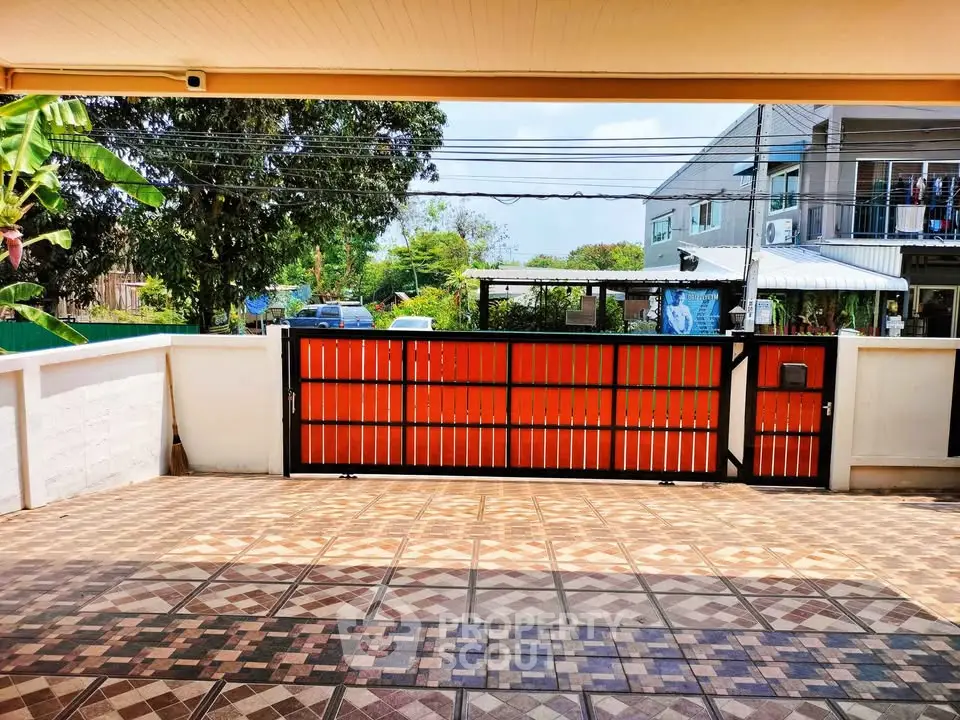 Spacious tiled patio with modern gate and lush greenery view.