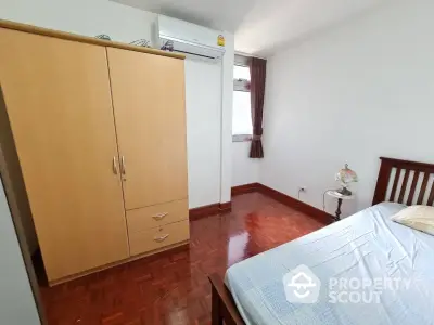 Cozy bedroom with wooden flooring and ample natural light, featuring a wardrobe and air conditioning.