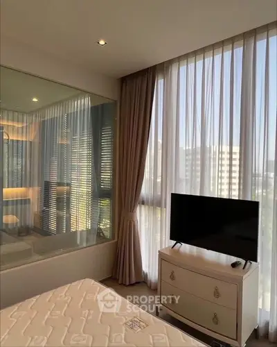 Modern bedroom with large window and TV, featuring elegant curtains and a stylish dresser.