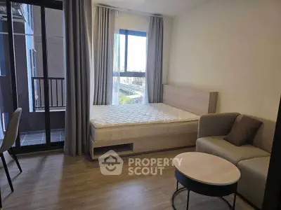Modern studio apartment with bed, sofa, and balcony access in a bright, cozy setting.