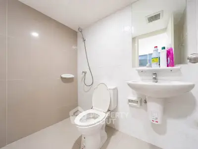 Modern bathroom with sleek fixtures and neutral tiles, featuring a toilet, sink, and shower area.