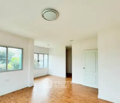 Spacious empty room with wooden flooring and large windows, ideal for customization.