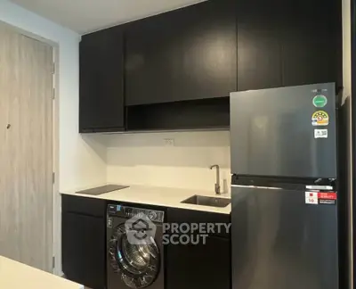 Modern kitchen with sleek black cabinets, integrated washing machine, and stainless steel fridge.
