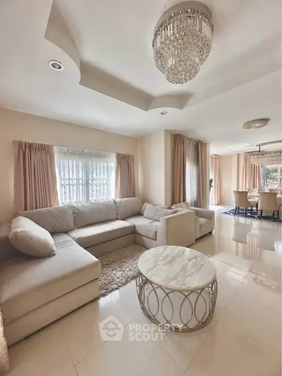 Elegant living room with plush sectional sofa and chic chandelier in a spacious, sunlit interior.