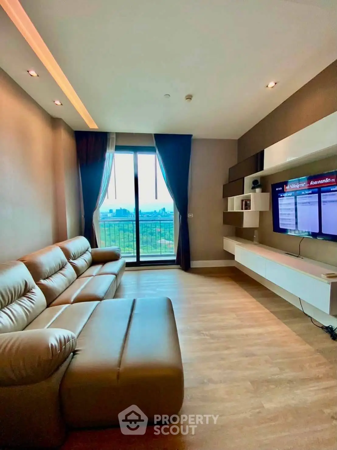 Modern living room with leather sofa and wall-mounted TV, featuring a scenic balcony view.