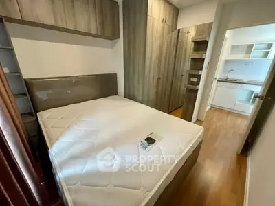 Cozy bedroom with modern wooden cabinetry and adjacent kitchenette in a compact apartment.