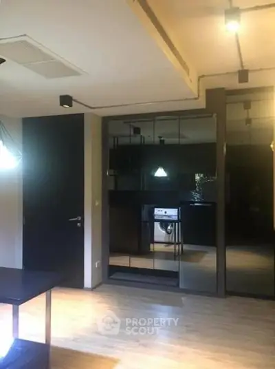 Modern apartment interior with sleek design and wooden flooring, featuring a mirrored wall and built-in appliances.