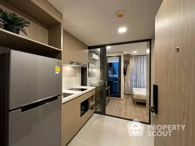 Modern compact kitchen with sleek appliances seamlessly leads to a cozy bedroom, showcasing efficient use of space in a stylish urban apartment.