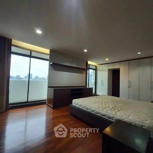Spacious modern bedroom with large windows and city view, featuring wooden flooring and built-in wardrobes.