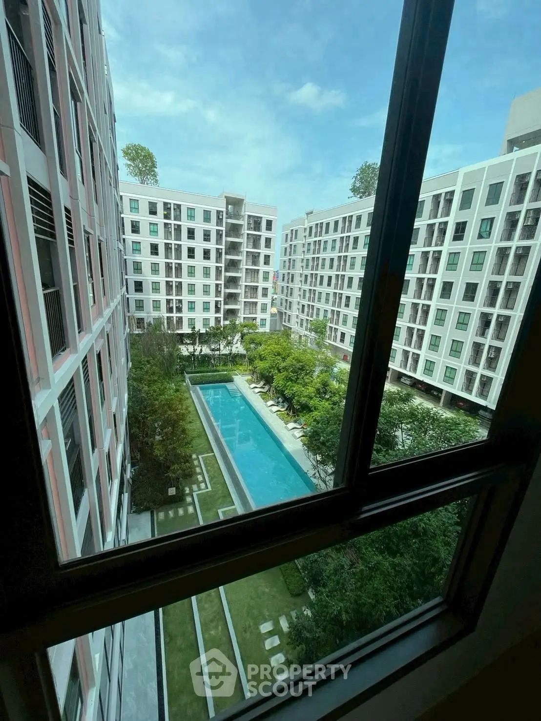 Stunning view of modern apartment complex with pool and lush greenery from window.