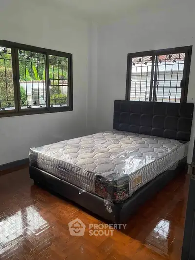 Spacious bedroom with new mattress and hardwood flooring, featuring large windows for natural light.