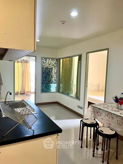Bright kitchen with open layout and dining area, featuring modern fixtures and a view into a cozy bedroom.