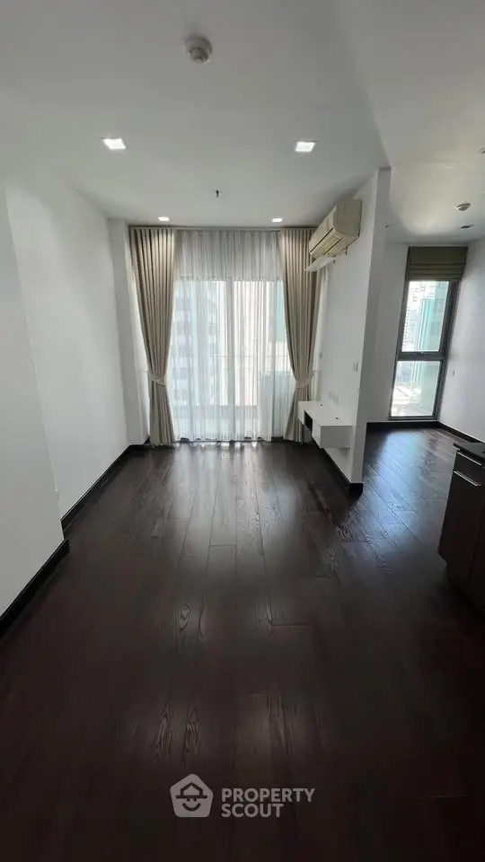 Spacious modern living room with dark wood flooring and large windows offering city views.