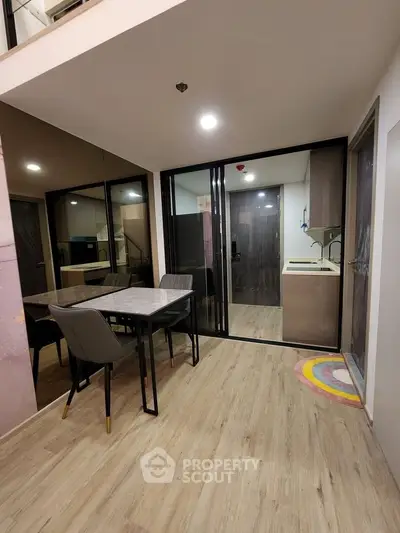 Modern dining area with sleek glass doors leading to a compact kitchen, featuring stylish flooring and contemporary furniture.