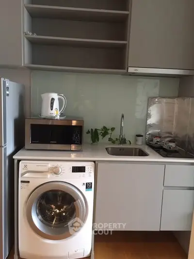 Modern kitchen with washing machine, microwave, and sleek cabinetry in compact layout.