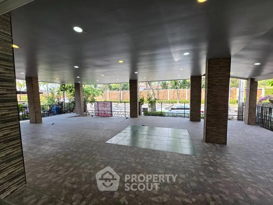 Spacious covered outdoor area with tiled flooring and garden view, perfect for gatherings.