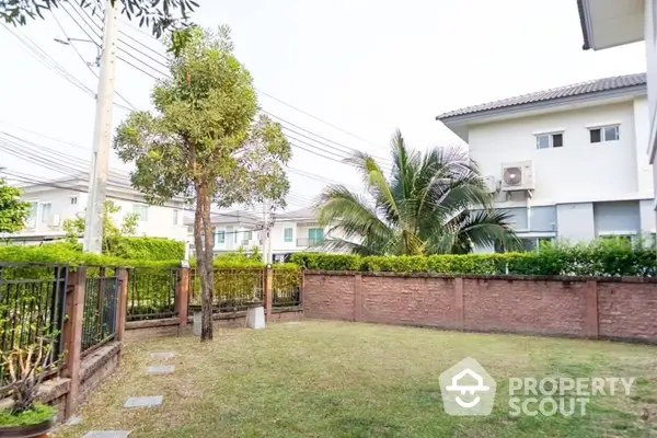 Spacious garden area with lush green lawn, surrounded by a high brick wall and mature trees, offering privacy and tranquility in a suburban neighborhood.