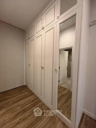 Spacious bedroom with elegant built-in wardrobe and mirrored door, featuring stylish wood flooring.