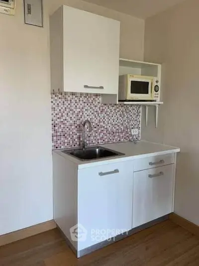 Compact kitchen with modern white cabinetry and mosaic backsplash, featuring a microwave and stainless steel sink.