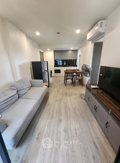 Modern living room with sleek furniture and open kitchen layout, featuring a cozy sofa and dining area.