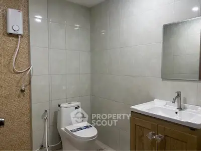 Modern bathroom with sleek fixtures and tiled walls, featuring a toilet, sink, and shower.