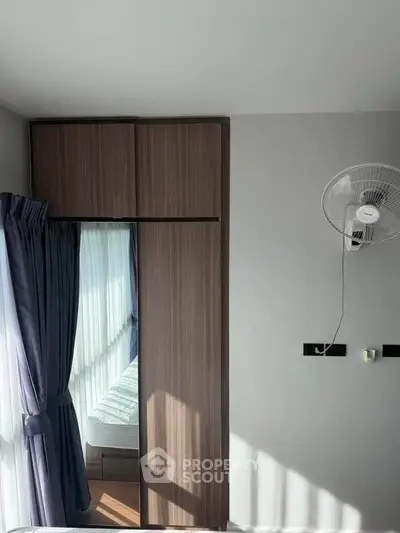 Modern bedroom with sleek wardrobe and wall-mounted fan, featuring natural light through large window.