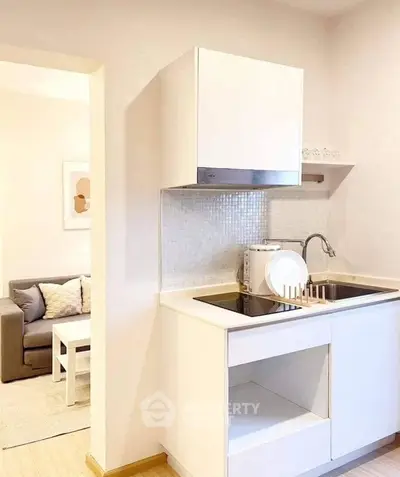 Modern compact kitchen with sleek white cabinetry and cozy living room view.