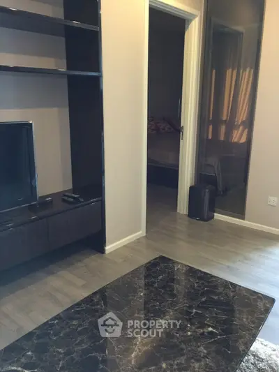 Modern living room with sleek TV unit and marble coffee table, leading to a cozy bedroom.