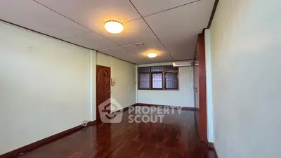 Spacious empty room with wooden flooring and classic window design.