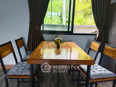 Charming dining area with wooden table and chairs, featuring a lush green view through the window.