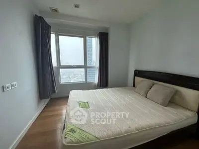 Spacious bedroom with large window offering city views, featuring a comfortable bed and elegant curtains.