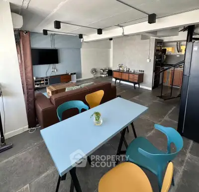 Modern industrial-style living room with colorful dining chairs and open kitchen layout.