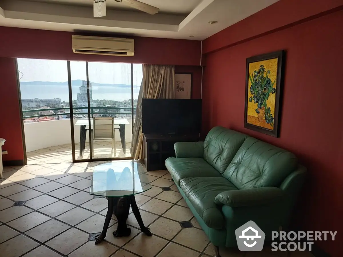 Spacious living room with a vibrant red wall, comfortable green leather sofa, and a captivating city view through the balcony doors.