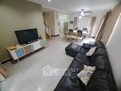 Spacious living room with modern decor and dining area, featuring a large leather sofa and flat-screen TV.