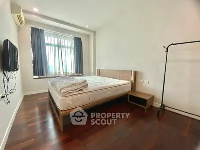 Spacious bedroom with hardwood floors and large window in modern apartment