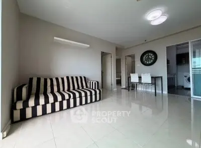 Spacious living room with modern striped sofa and dining area in open layout apartment.