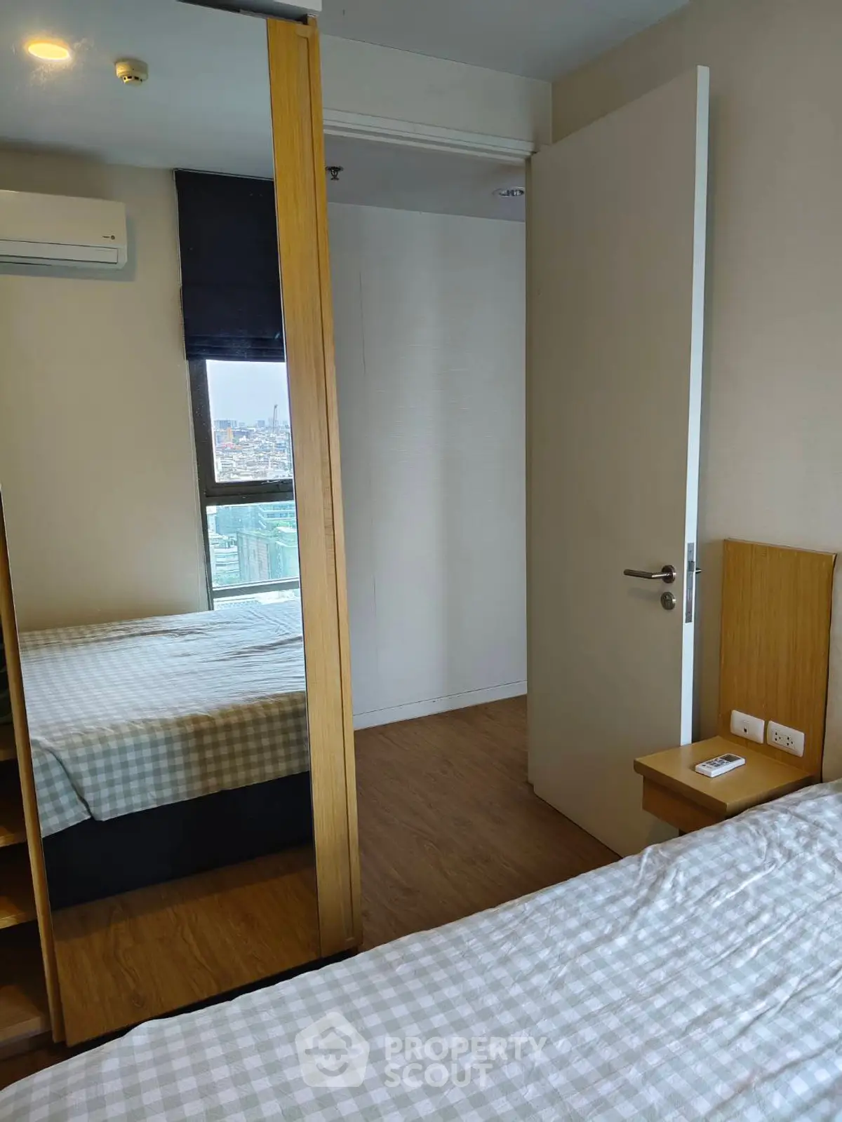 Cozy bedroom with mirrored wardrobe and city view, featuring modern decor and natural light.