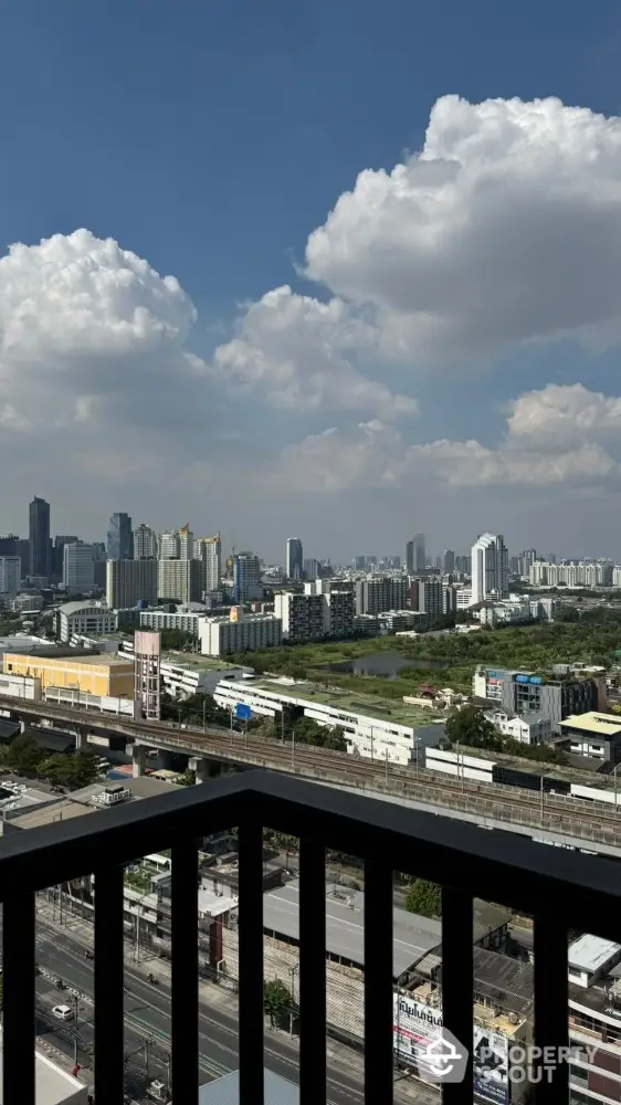 Stunning cityscape view from high-rise balcony with clear blue sky and clouds.