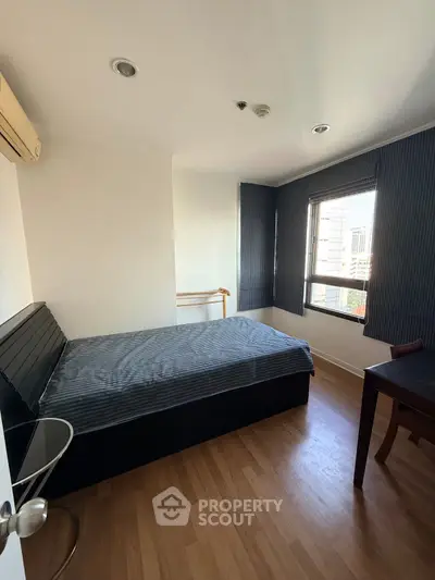 Cozy bedroom with wooden flooring and natural light from large windows.