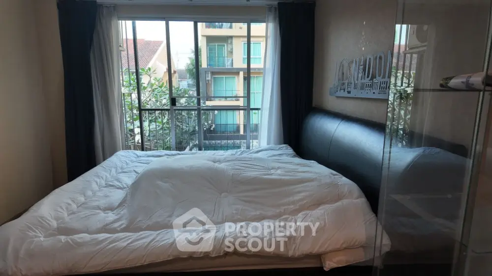 Cozy bedroom with large window and modern decor, offering natural light and a comfortable atmosphere.