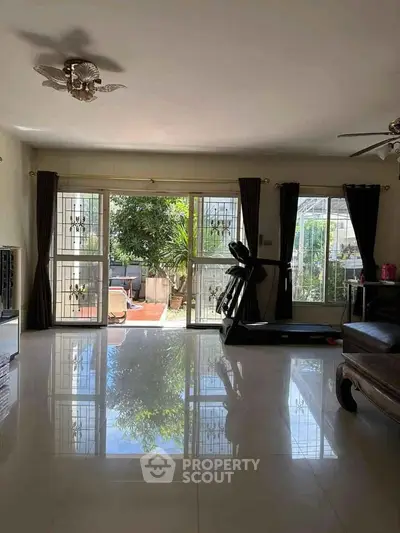 Spacious living room with large windows and garden view, featuring a treadmill and elegant decor.