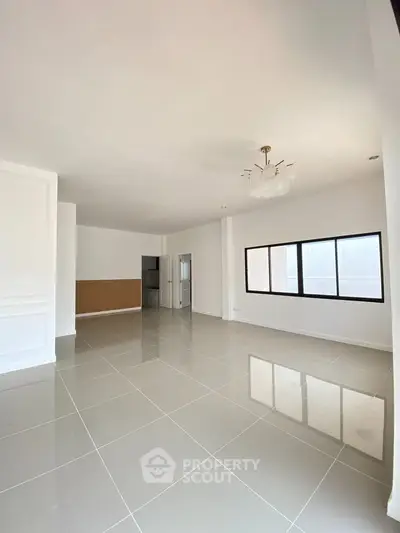 Spacious modern living room with large windows and elegant chandelier in a minimalist design.
