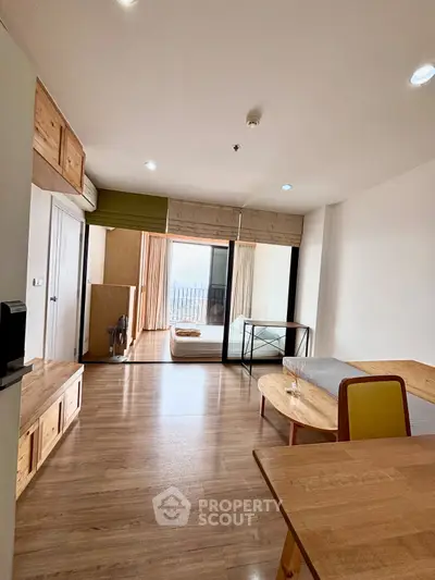 Spacious modern living room with wooden flooring and large windows offering natural light and a view.