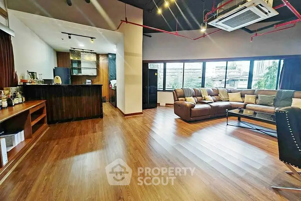 Spacious modern living room with wooden flooring and large windows offering natural light.