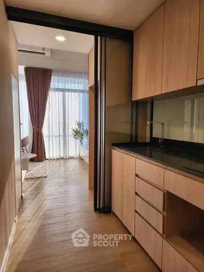 Modern kitchen with sleek wooden cabinetry and open layout leading to a bright living area.