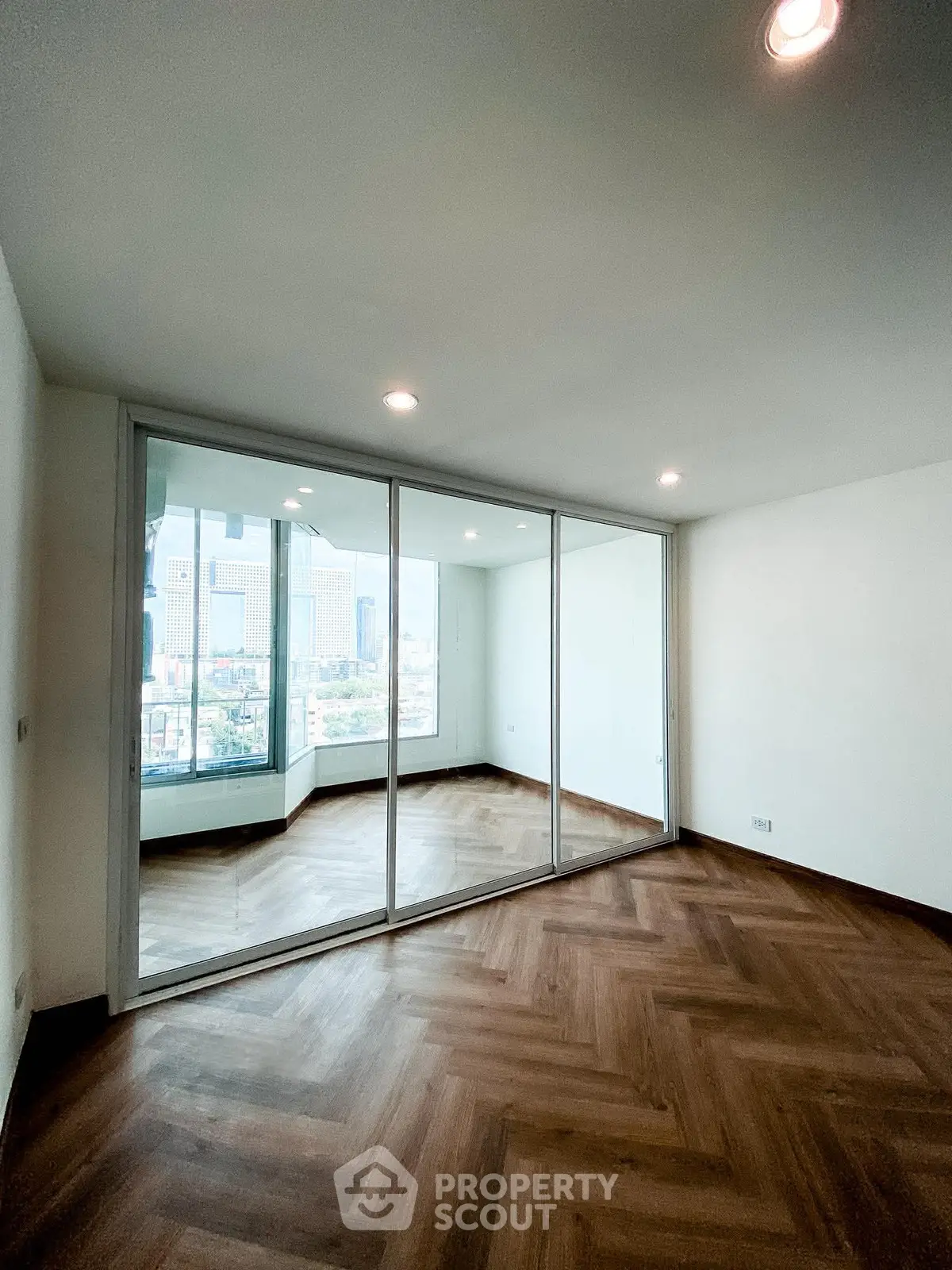 Spacious room with large windows offering a stunning city view and elegant wooden flooring.