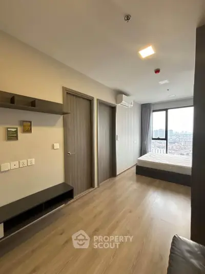 Modern bedroom with large window offering city view, featuring sleek wooden flooring and minimalist design.