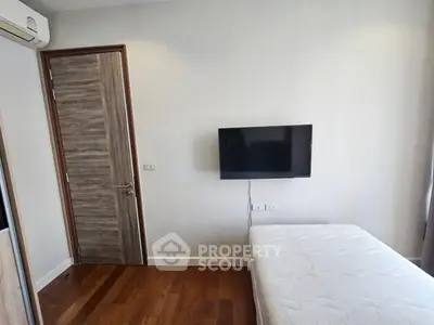 Modern bedroom with wall-mounted TV and wooden flooring in a stylish apartment.