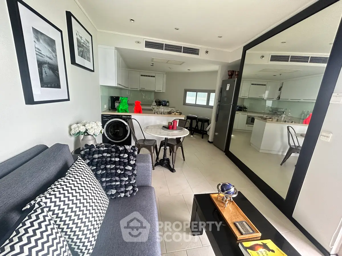 Modern living room with open kitchen, stylish decor, and large mirror enhancing space.