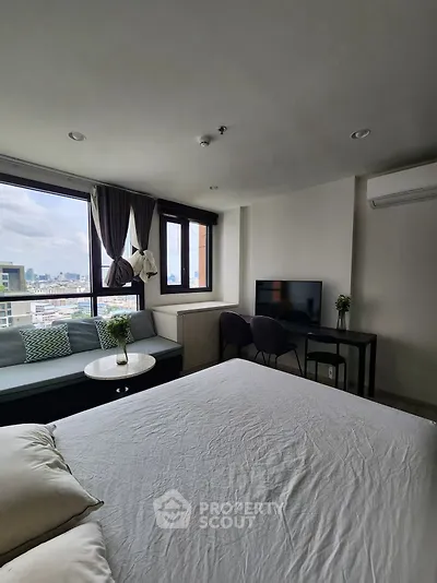 Modern bedroom with city view, featuring cozy seating area and sleek TV setup.